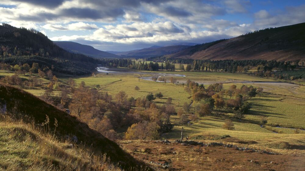 Looking across a wide glen, with a river snaking through the middle. Tall mountains rise either side.