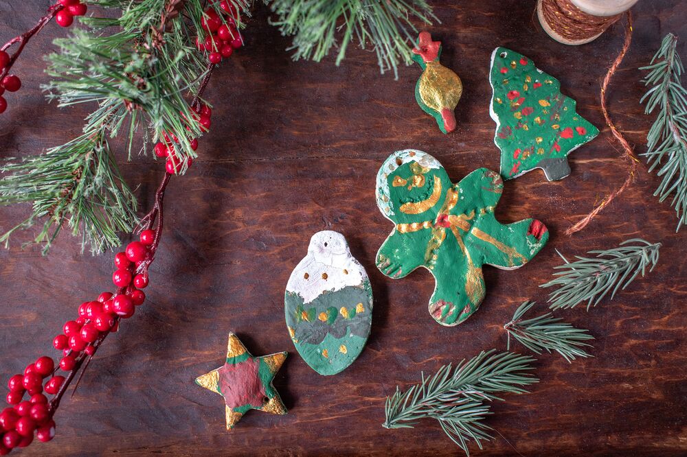 Hand-painted salt dough decorations in the shape of a star, bauble, gingerbread man and a Christmas tree lie on a wooden table.