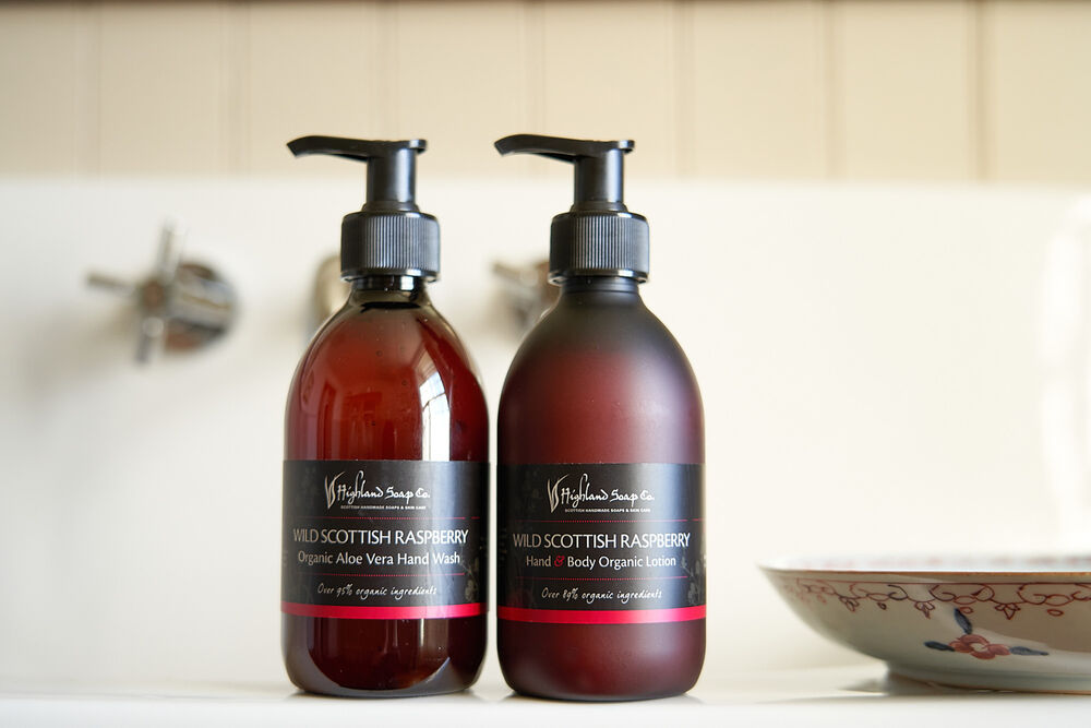 Two dark red soap bottles on a sink next to a decorated soap dish.