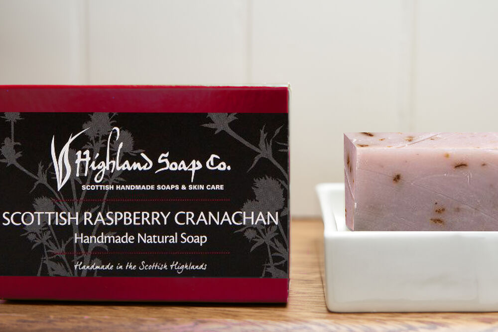 A dark pink box with a black label next to a pink bar of soap in a soap dish.