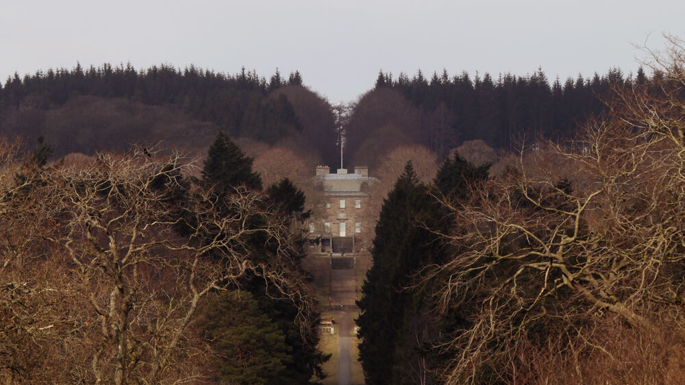 An aerial view looking down a long tree-lined avenue towards the grand Georgian Haddo House.