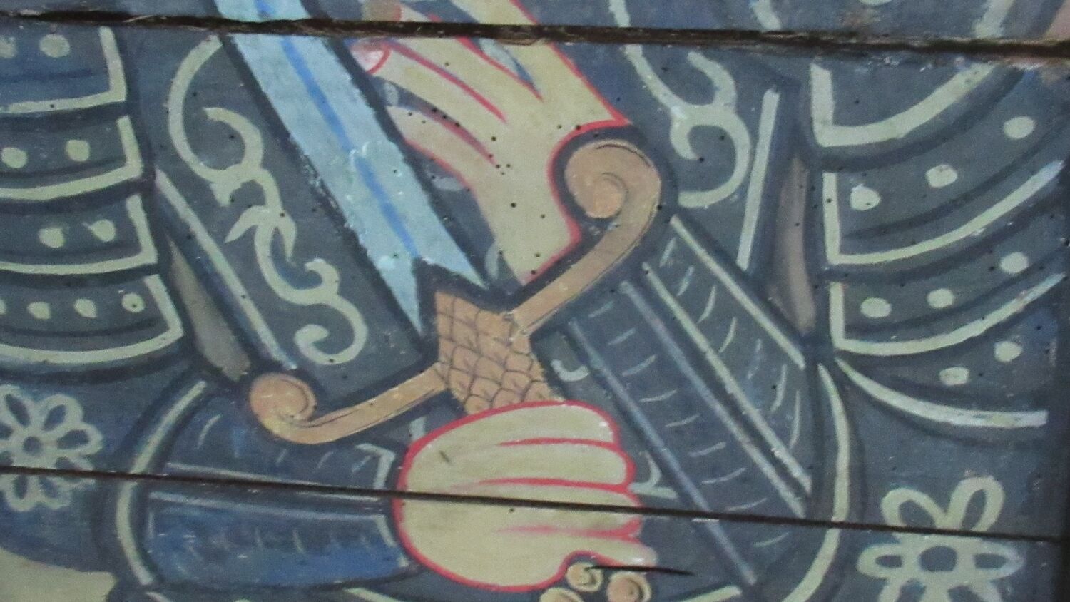 A close-up image detailing the medieval painting of a knight's torso, wearing armour and holding a sword across his body.