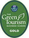 A green oval badge from the Green Tourism Business Scheme showing a Gold award. There is a blue roundel at the top with an illustration of a teal and purple thistle in it.